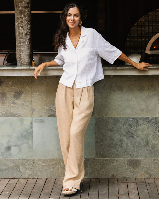 Woman in a white top and beige pants standing against a stone wall.