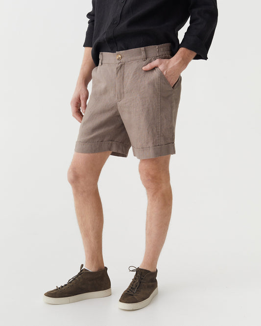 Person wearing taupe shorts and dark shoes on a white background