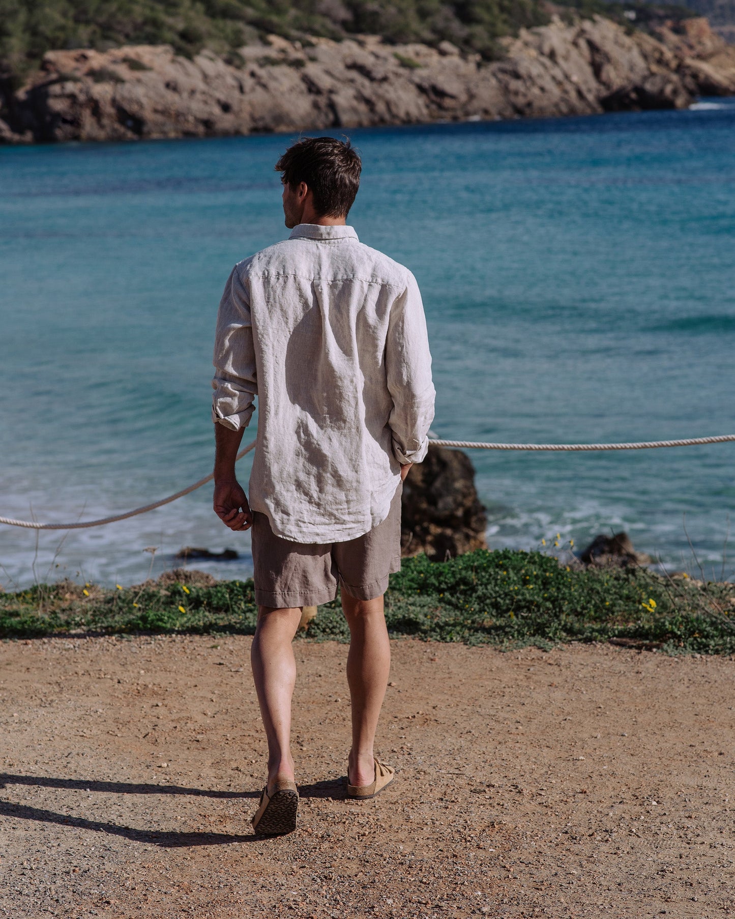 Man standing by a body of water wearing a light-colored shirt and shorts.