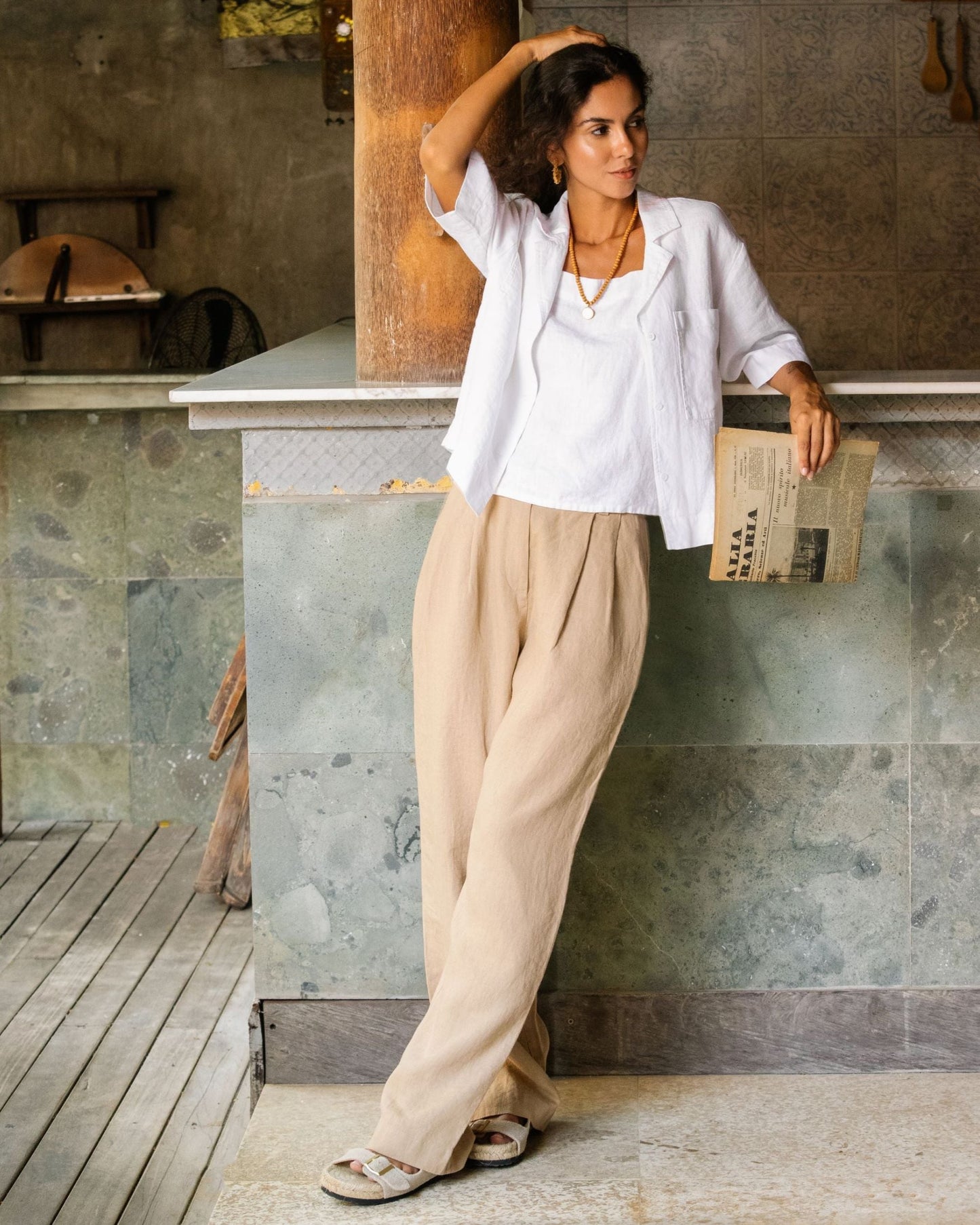 Woman in white shirt and beige pants leaning against a stone wall.