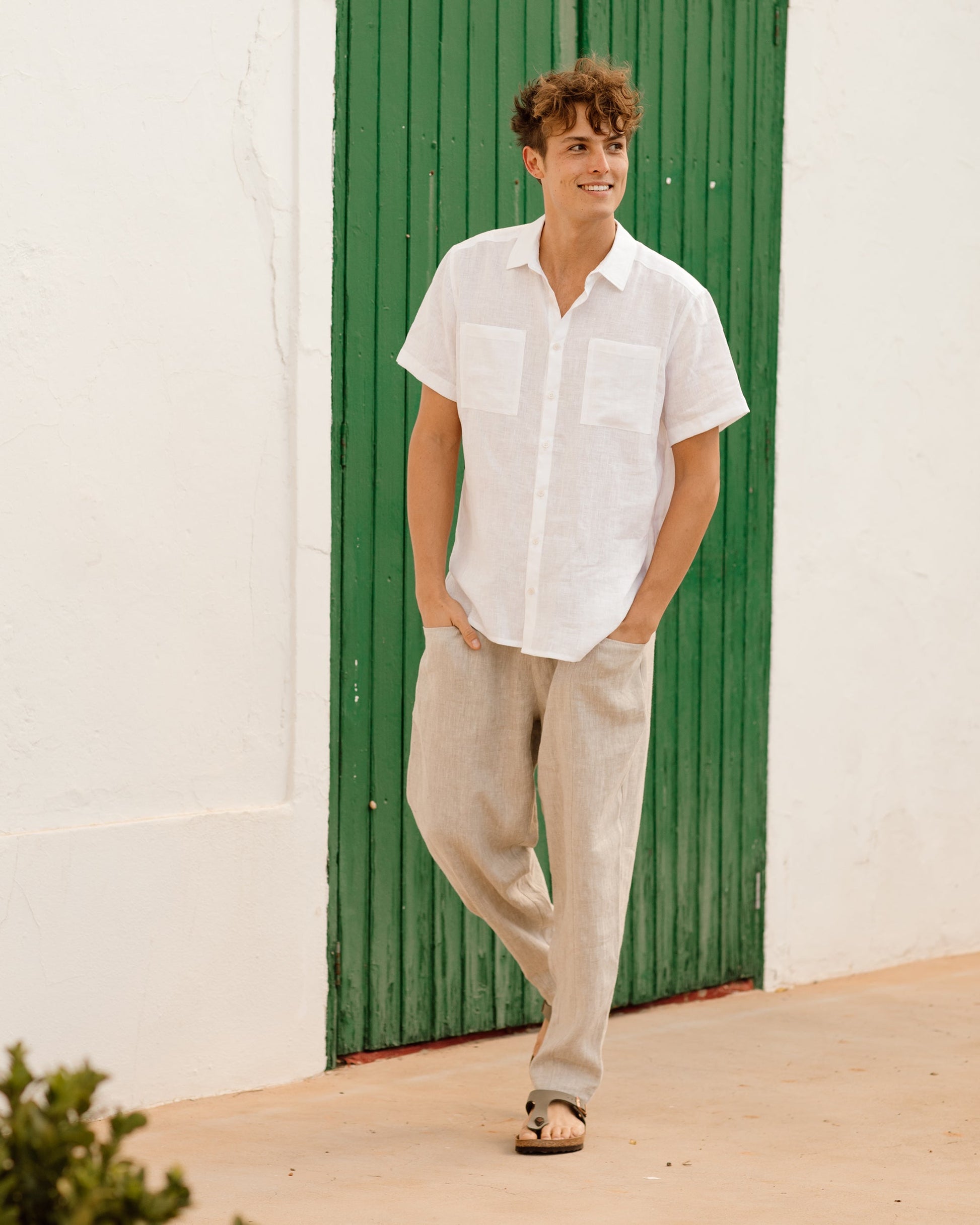 Man wearing a white shirt and beige pants standing in front of a green door.