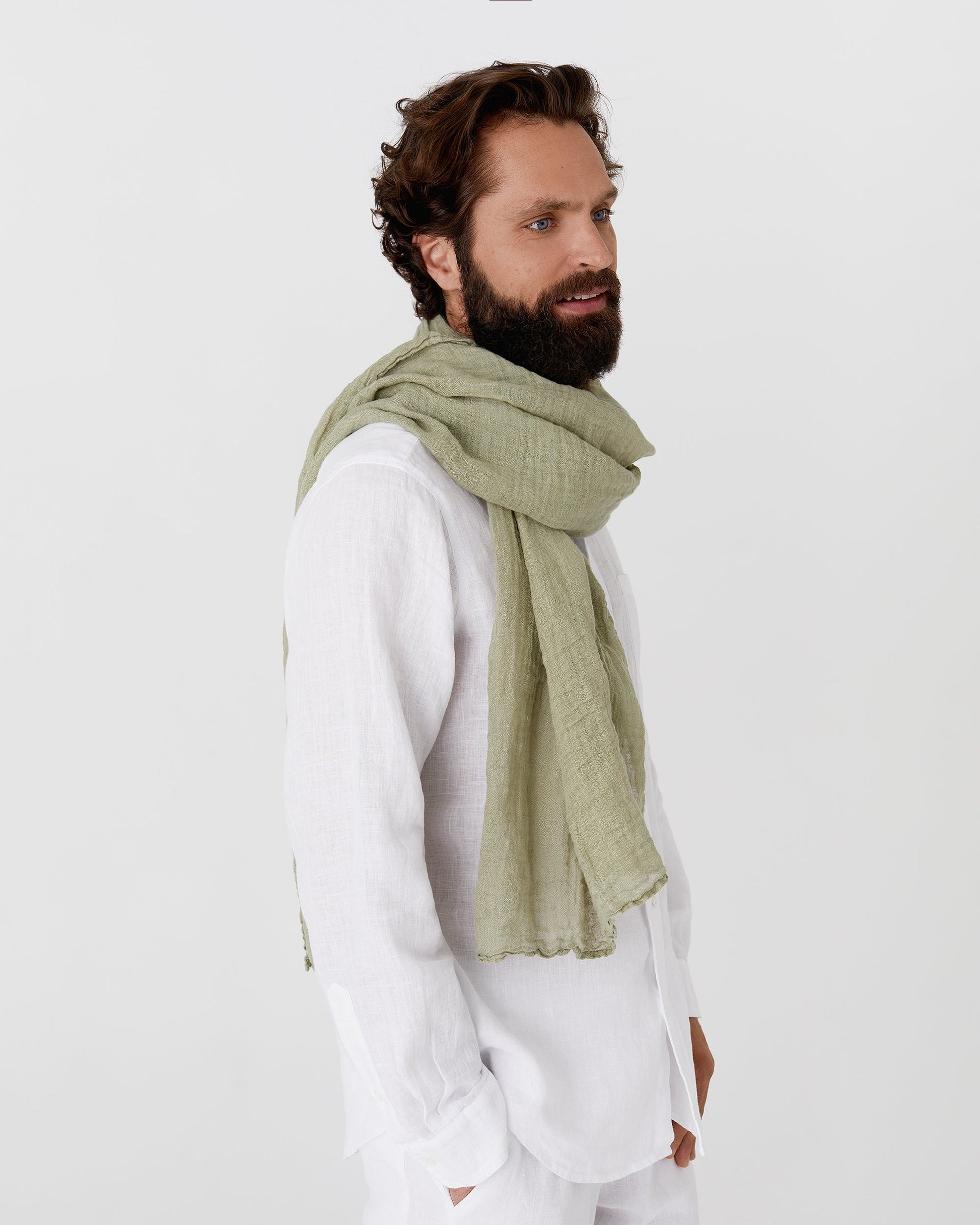 Man wearing a green scarf and white outfit on a plain background