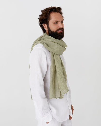 Man wearing a green scarf and white outfit on a plain background
