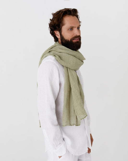 Man wearing a green scarf and white outfit on a plain background
