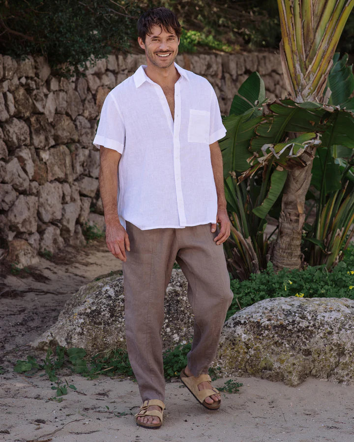 Man wearing a white shirt and beige pants standing in a natural setting with rocks and plants.
