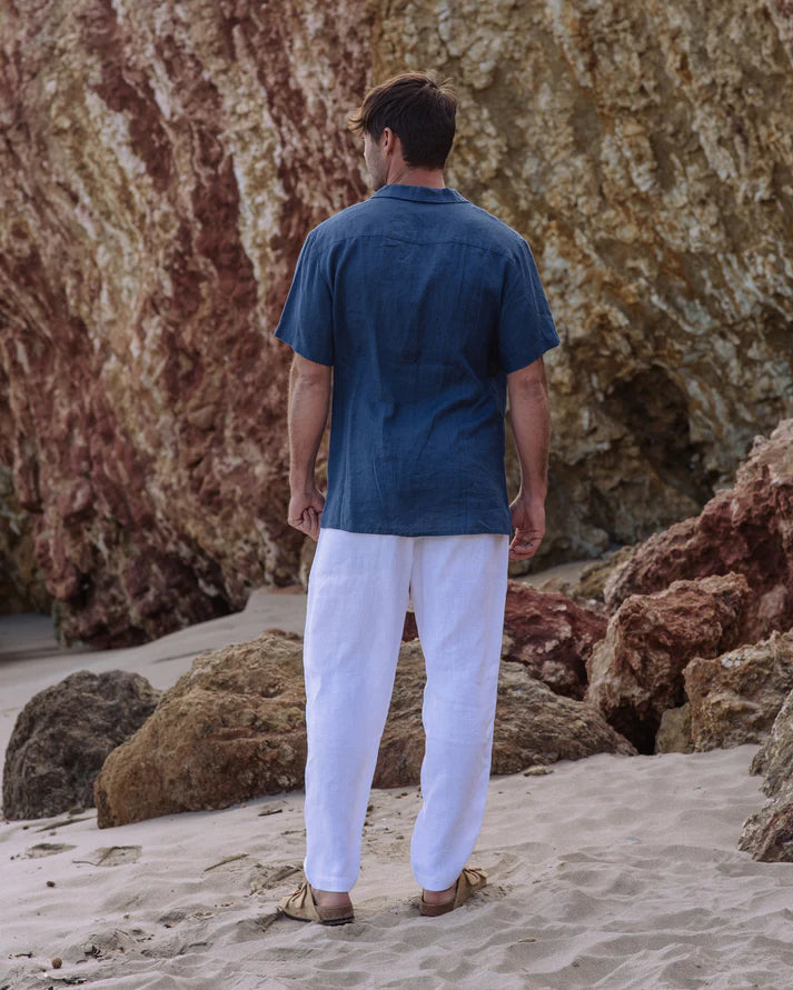 Man in a blue shirt and white pants standing on a rocky beach.