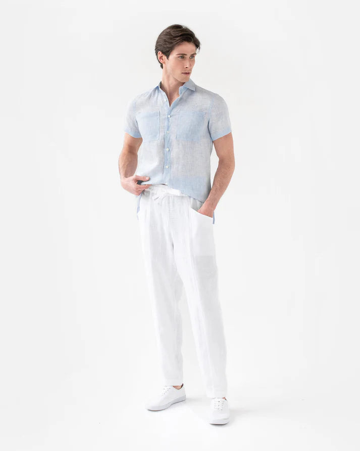 Man wearing a light blue patterned shirt and white pants on a white background