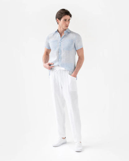 Man wearing a light blue patterned shirt and white pants on a white background