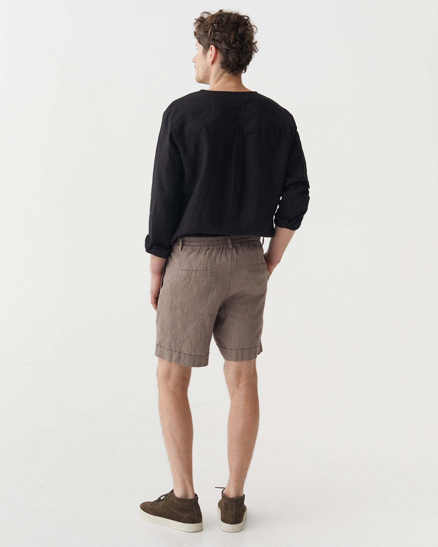 Man wearing a black sweater and taupe shorts on a white background
