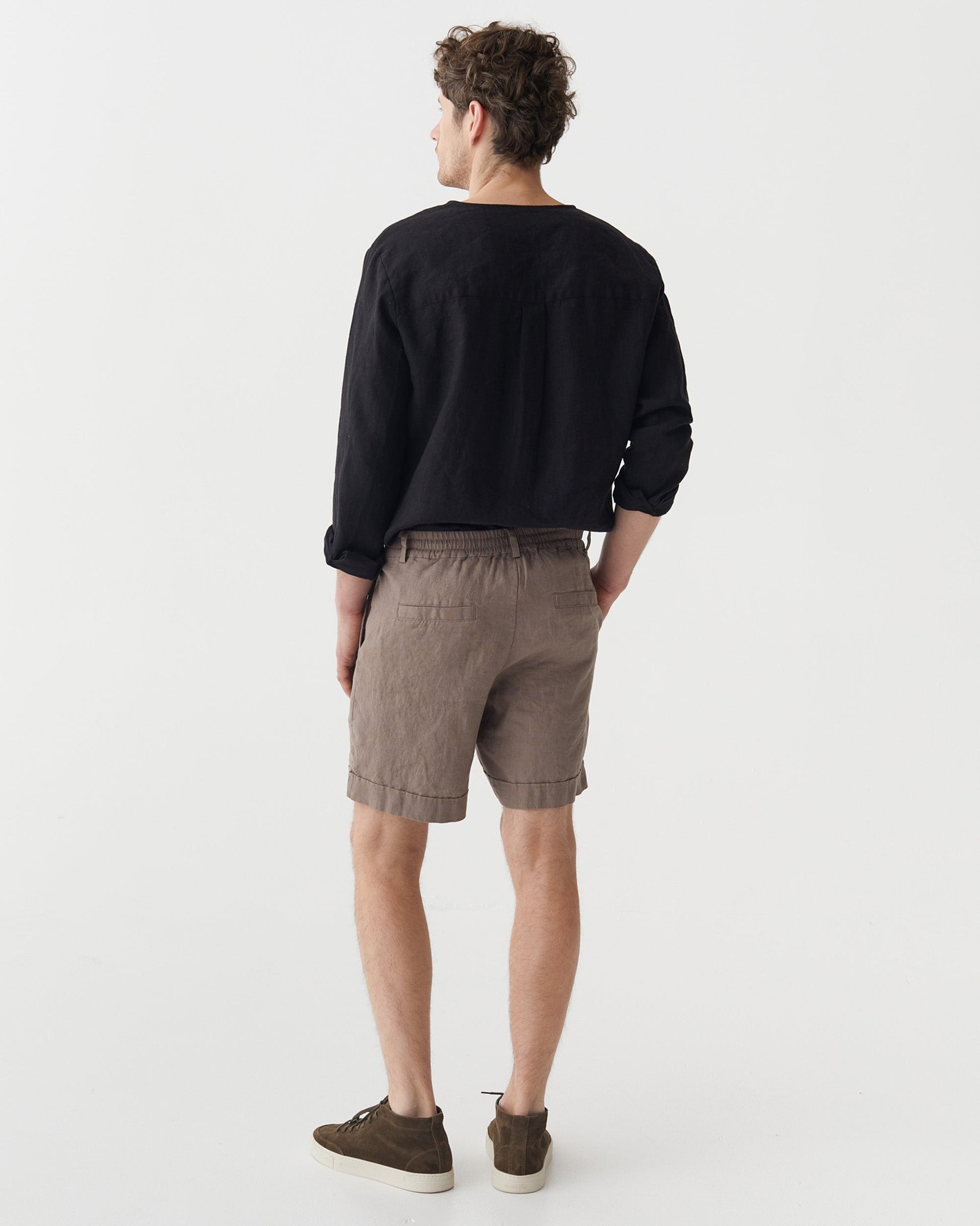 Man wearing a black sweater and taupe shorts on a white background