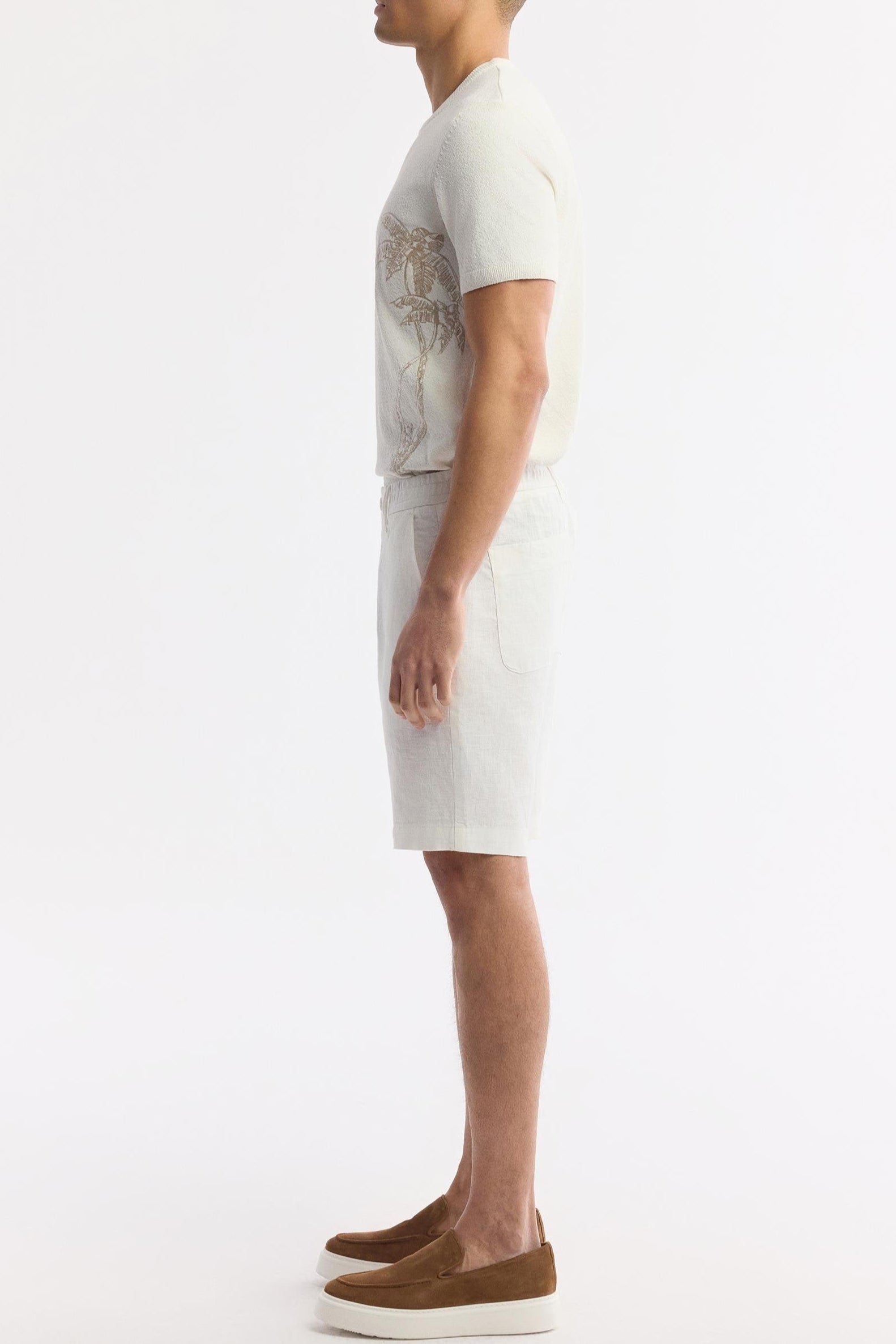 Model side view showcasing relaxed fit of white linen shorts