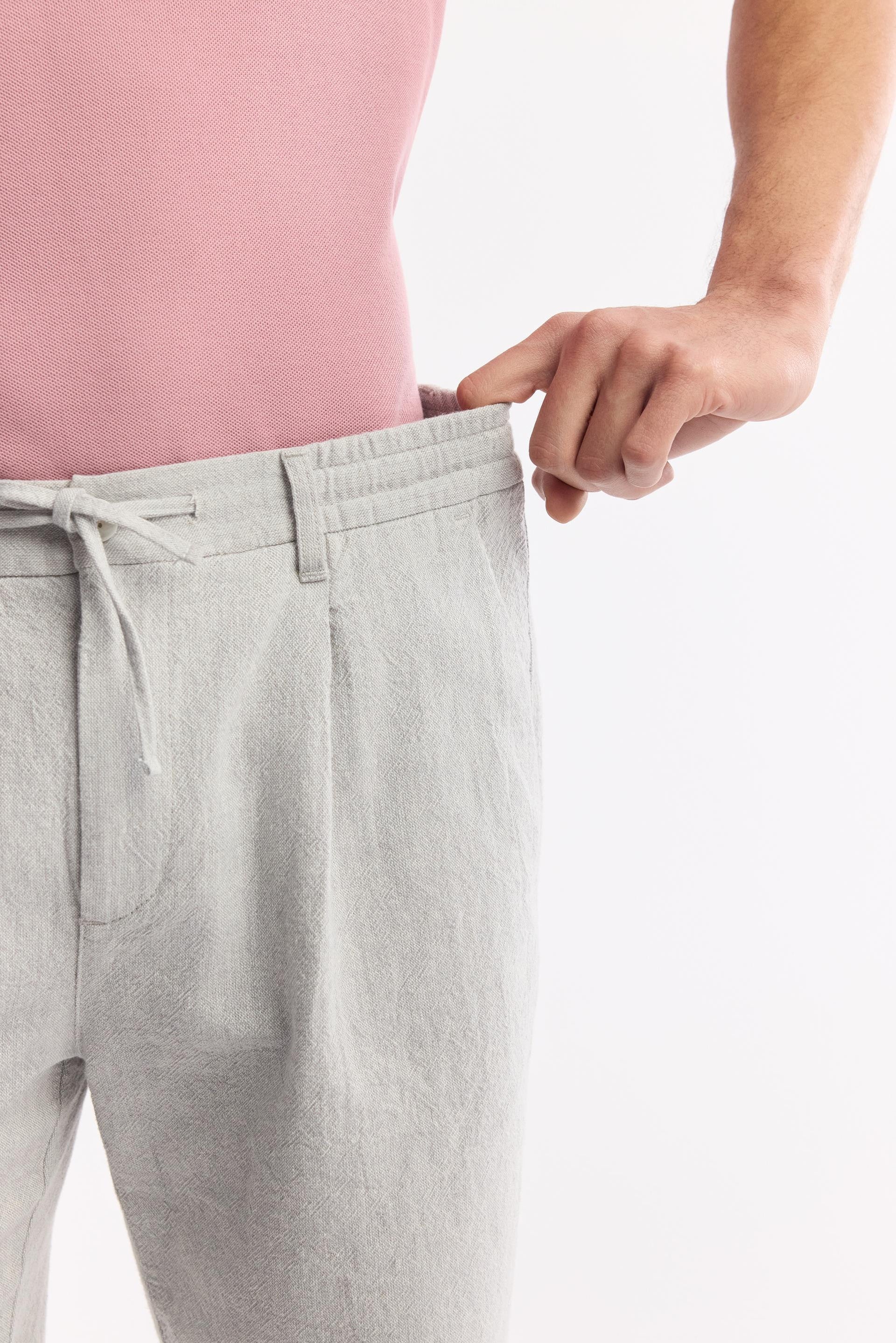 Hand stretching elastic waistband on men’s gray linen shorts – Swiftyle