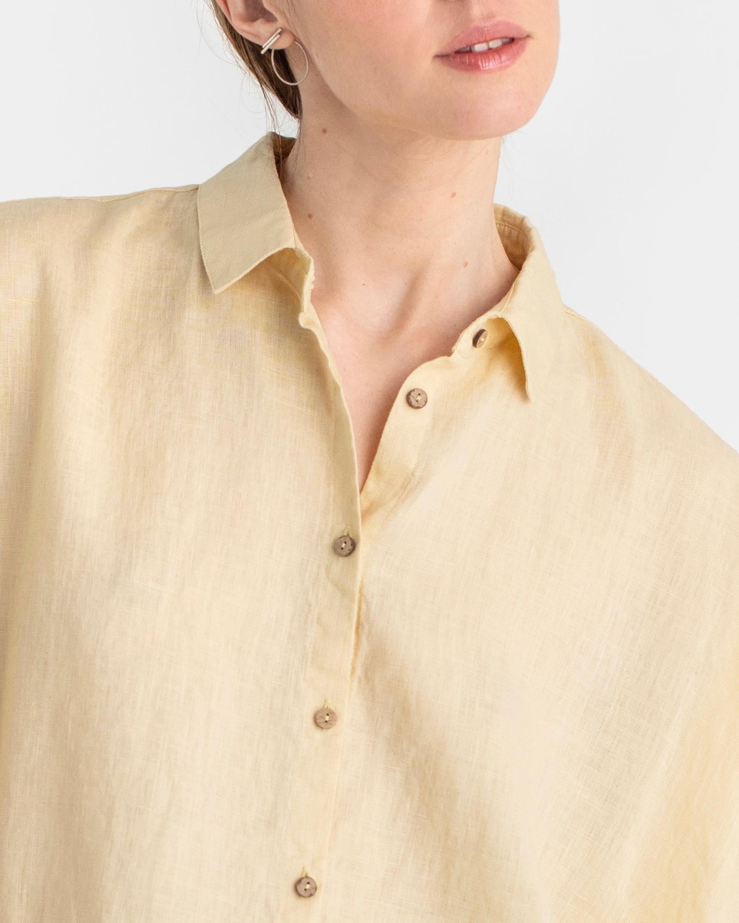Close-up of a person wearing a light yellow button-up shirt against a white background