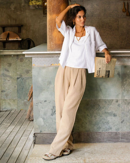 Woman in white shirt and beige pants leaning against a stone wall.