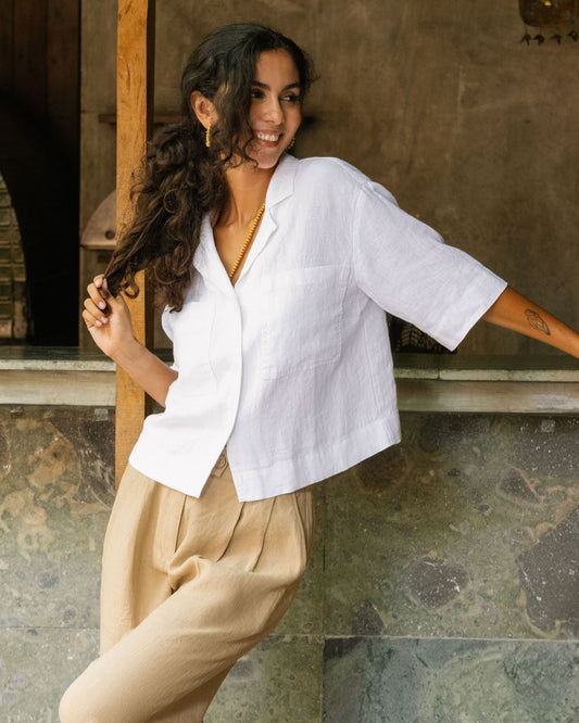 Woman wearing a white top and beige pants standing against a textured wall.